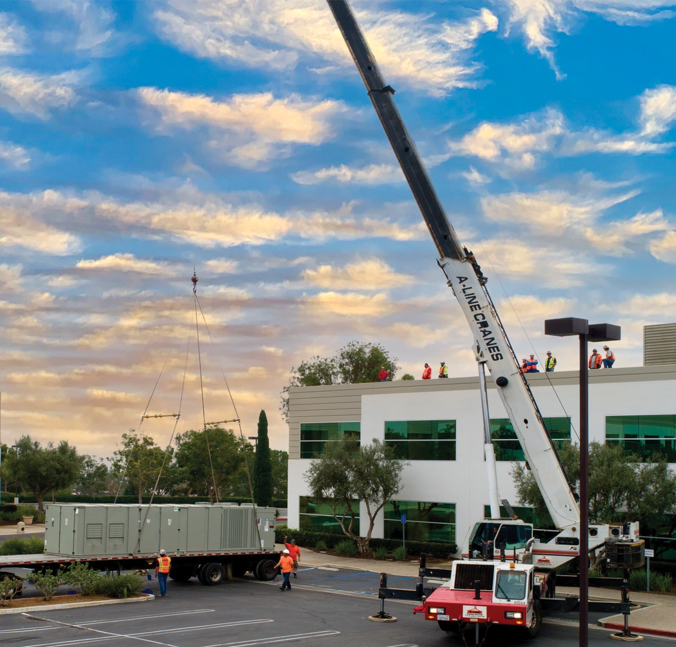 Crane lifting a commercial HVAC unit onto a two story building on a beautiful day