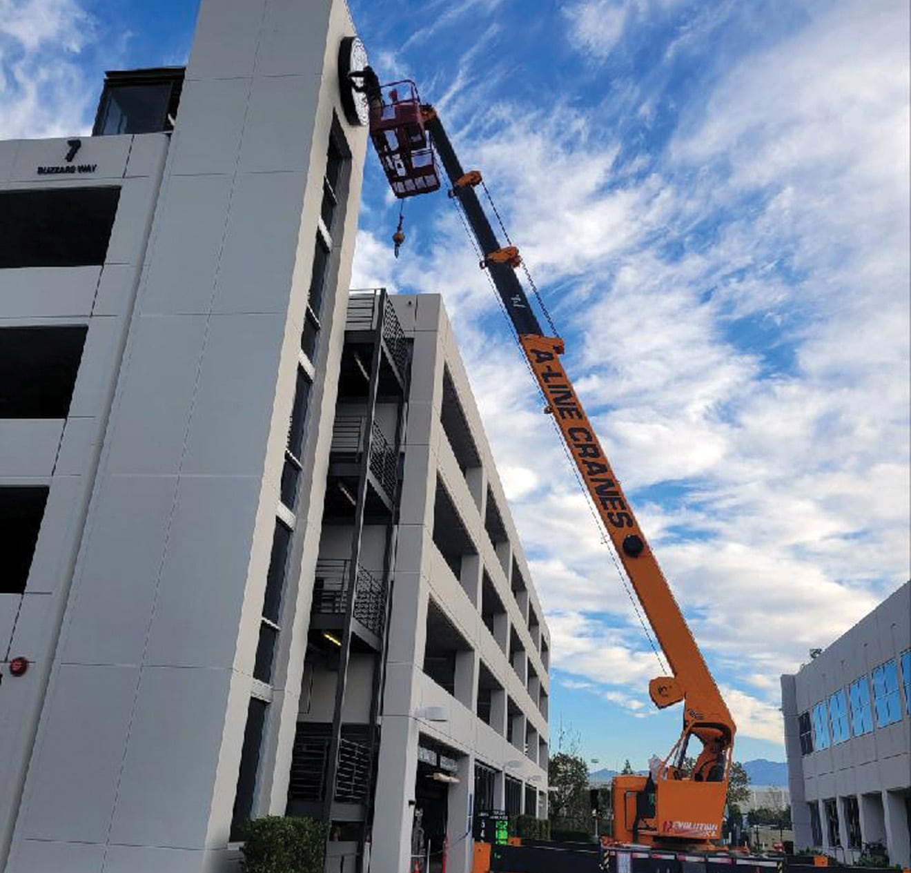 Crane lifting man in man basket to change sign on a building