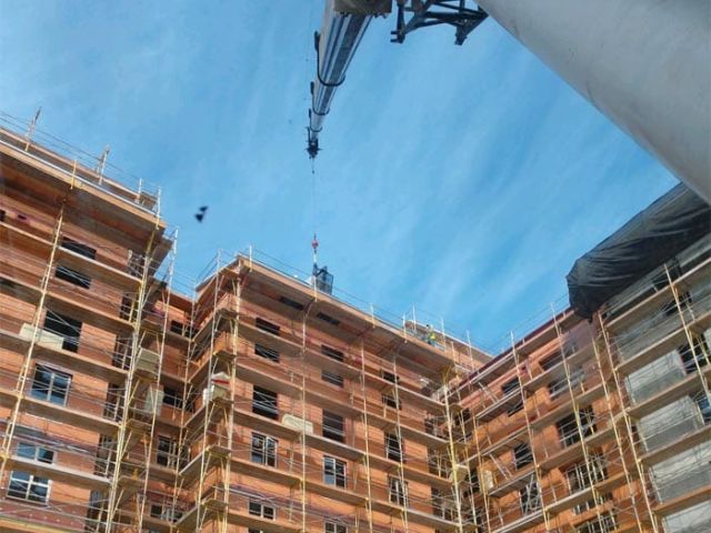 Construction crane lifting building materials onto roof in southern california