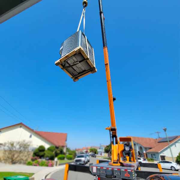 An orange truck crane lifting an HVAC air conditioner unit from the street over a residents home in california
